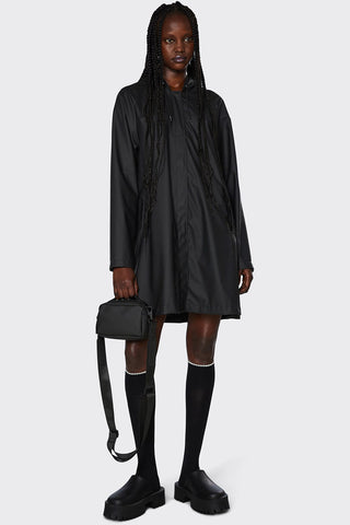 Model wearing lightweight black waterproof A-Line rain jacket by RAINS. 