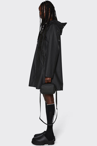 Side view of model wearing lightweight black waterproof A-Line rain jacket by RAINS. 
