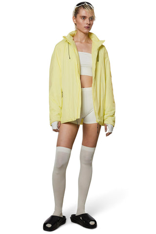 Model wearing yellow (straw) insulated waterproof RAINS Fuse jacket. 