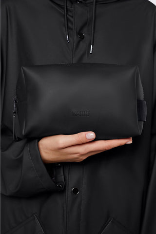 Model holding waterproof unisex black RAINS wash bag. 